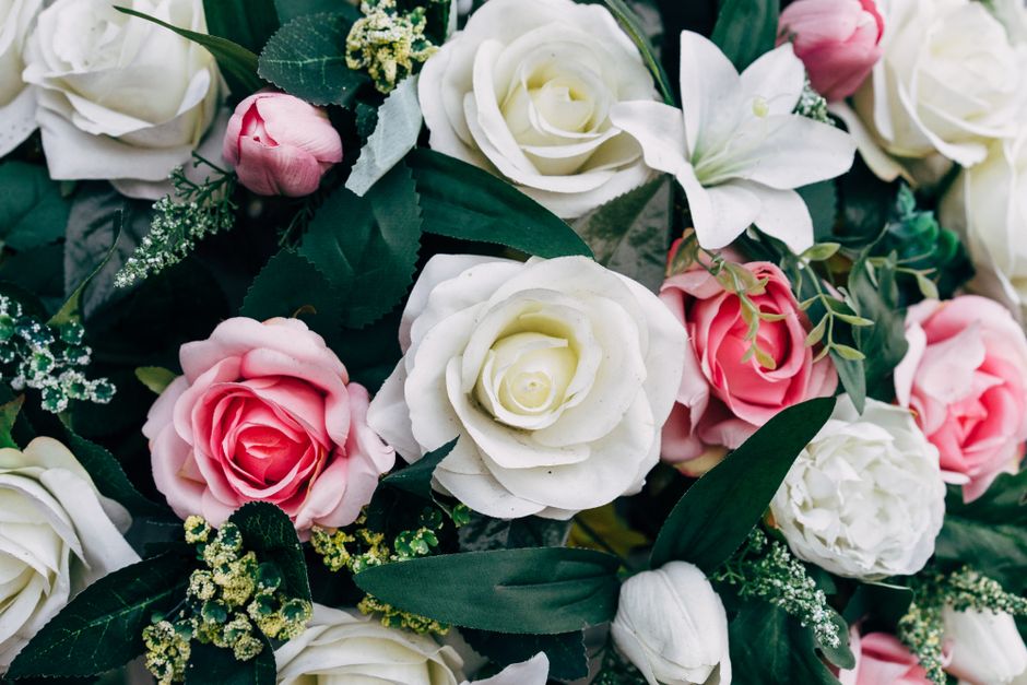 A close-up of a floral arrangement featuring a variety of artificial roses in soft pink, creamy white, and light blush tones, complemented by green foliage and small sprigs of delicate white filler fl